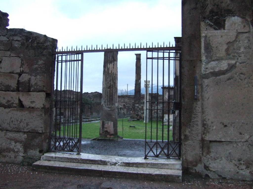 VII.7.32 Pompeii. December 2005. Entrance doorway on Via Marina. 
According to Cooke Cockburn and Donaldson: “However splendid in their general arrangements, the columns of the peribolus are capricious in taste and decoration. The capitals are of stucco, of the Corinthian order, with a single row of leaves covering a capital originally Doric; the entablature is of tufo, once Doric, but converted to accord with the capital by a thick coat of plaster, in a grotesque style and painted. The walls of the court are covered with paintings of the most interesting description. They are in vivid colours and represent generally landscapes, views of country houses, interiors of rooms with male and female figures; in several compositions figures are drawn sporting among themselves, sacrificing to Priapus, contending with crocodiles, or occupied in domestic duties; nor must we omit a painting of Hector tied to the car of Achilles, and one of Agamemnon and Achilles. The sanctuary itself now presents only its four dark walls, raised on an elevated and dismantled basement, in former times enriched with marbles; the portico completely surrounded the cella, having six columns in front, and in all probability eleven on the flanks, agreeing in this respect with the rules of Vitruvius.
Withinside is the rough construction for the altar, and the pavement is a very elegant mosaic, the centre compartment consisting of green, white and black marbles, and the border of a Greek meander of black, white and red mosaic.  The walls, as well as the steps, retain every appearance of the fatal effects of the earthquake, being shattered, out of level, and displaced. At the end of the court, opposite the entrance, is a small chamber, which possesses an invaluable picture of Bacchus and Silenus, the former holding the thyrsus in one hand and a vase in the other; Silenus appears with his lyre instructing the god. A small niche is in the wall, apparently for the reception of a statue or lares.”
See Cooke Cockburn Donaldson: Pompeii, Pt 1, 1827, (p.55)