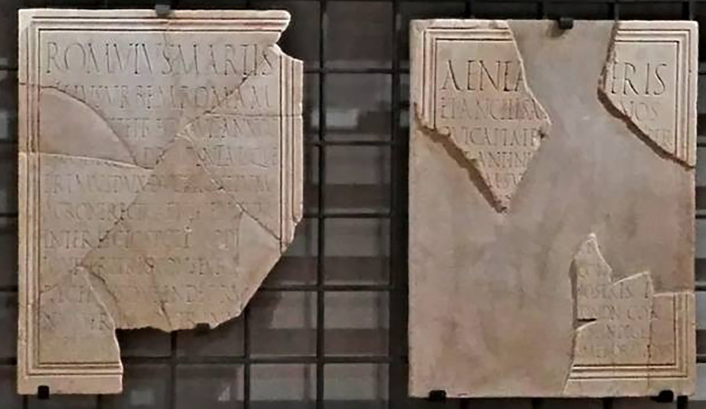 VII.9.1 Pompeii. June 2017. Marble dedication plaques to Romulus (left) and Aeneas (right) found near the so-called Building of Eumachia in 1817.
Now in Naples Archaeological Museum. Inventory numbers 3820 (Romulus) and 3819 (Aeneas).
Photo (detail) courtesy of Giuseppe Ciaramella.