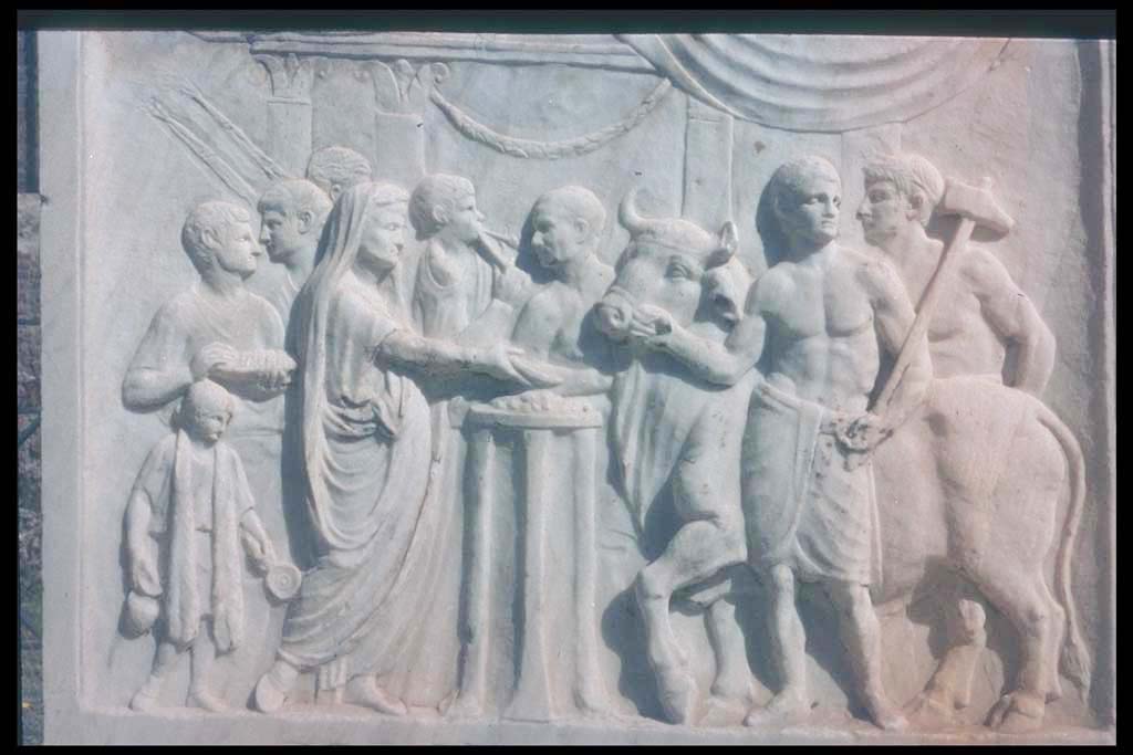 VII.9.2 Pompeii. Sacrificial scene on West side of altar.
According to Mau, a priest with a toga drawn over his head pours a libation from a shallow bowl or patera onto an altar which is in the form of a tripod. 
With him at the left are two lectors with their bundles of rods, a flute player, two boys – camilli - carrying the utensils for the sacrifice, and also an attendant.
At the right the victimarius or slayer and an assistant are bringing a bull to the altar for sacrifice.
In the background is a Tetrastyle temple, “doubtless the temple before us; the scene represents the dedicatory exercises.”
As the sacrifice is a bull it means the temple must have been dedicated to an emperor during his lifetime.
See Mau, A., 1907, translated by Kelsey F. W. Pompeii: Its Life and Art. New York: Macmillan. (Pages 106-7).
Photographed 1970-79 by Günther Einhorn, picture courtesy of his son Ralf Einhorn.