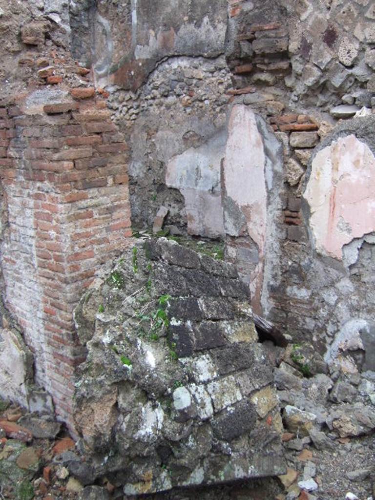 VII.10.3 Pompeii. December 2005. Doorway to room 4, in north-west corner of atrium.
The doorway would have led into a room, described as a triclinium, originally with flooring of a reddish cocciopesto. The door threshold was formed by two square slabs of travertine and inserted in its south end was a small slab of grey marble. Seen on each of the smooth surface of the slabs, was a circular recess for the fixing of the double-door hinges. (p.54)
The floor was upgraded to a black and white mosaic. The walls were redecorated in the IVth style. The black zoccolo (dado/plinth) showed alternative narrow panels with rosettes, in the centre were plants motifs. The middle zone on each wall showed an edicula panel, painted white which contained a pinax, no longer visible. The side panels were painted red, edged by a simple bordered band.
Studi della Soprintendenza archeologica di Pompei, 22: l”Insula VII, 10 di Pompei, by Angelo Amoroso, (p.54 and p.74) 
According to Bragantini, on the north-east side the mosaic was visible, whilst on the south-east side the cocciopesto was visible.
See Bragantini, de Vos, Badoni, 1986. Pitture e Pavimenti di Pompei, Parte 3. Rome: ICCD. (p.179)