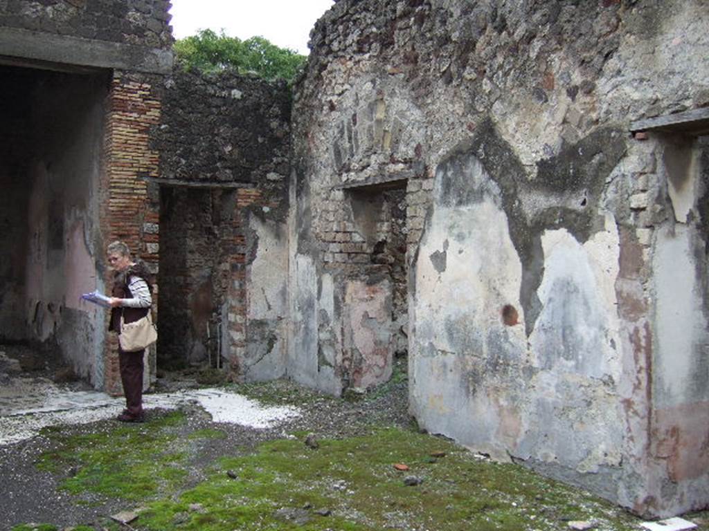 VII.10.3 Pompeii. December 2005. South-east corner of atrium with doorway to corridor 8 next to tablinum, and doorways to rooms 9 and 10 on south side of atrium. According to Breton, on the right of the tablinum was a corridor leading to a kitchen where a big iron bucket attached to a wall and the pipe used to fill it up, could still be seen. On the right was a painting of a woman holding a wand. 
See Breton, Ernest. 1870. Pompeia, Guide de visite a Pompei, 3rd ed. Paris, Guerin. 
According to Boyce, the woman held a rudder.
See Boyce G. K., 1937. Corpus of the Lararia of Pompeii. Rome: MAAR 14. (p.69, no.308)