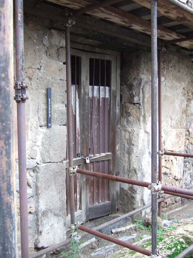 VII.12.28 Pompeii. December 2005. Entrance doorway.
According to Boyce, in this house was found a ruined lararium painting done on a white background.
He said it was not certain in which room the painting was seen.
Fiorelli placed it in the atrium, the Ann. Inst. and Helbig placed it in the kitchen.
In the west wall of the kitchen, a rectangular niche can be seen. Perhaps the painting was seen on the wall beside this niche?
Above the coils of a single serpent (female, according to Helbig) stood a Lar in green tunic and brown pallium.
The corresponding serpent and Lar on the other side had disappeared.
Helbig, 38; Ann.Inst., xxxv, 124, X; Fiorelli, Scavi, 105, No.17, Fiorelli, Descr., 291.
See Boyce G. K., 1937. Corpus of the Lararia of Pompeii. Rome: MAAR 14. (p.71, no.322) 
According to Giacobello –
The plastered arched niche was found in room (h) on the west wall, the room having decoration in the Fourth Style.
See Giacobello, F., 2008. Larari Pompeiani: Iconografia e culto dei Lari in ambito domestico. Milano: LED Edizioni, (p.292, no.C17)