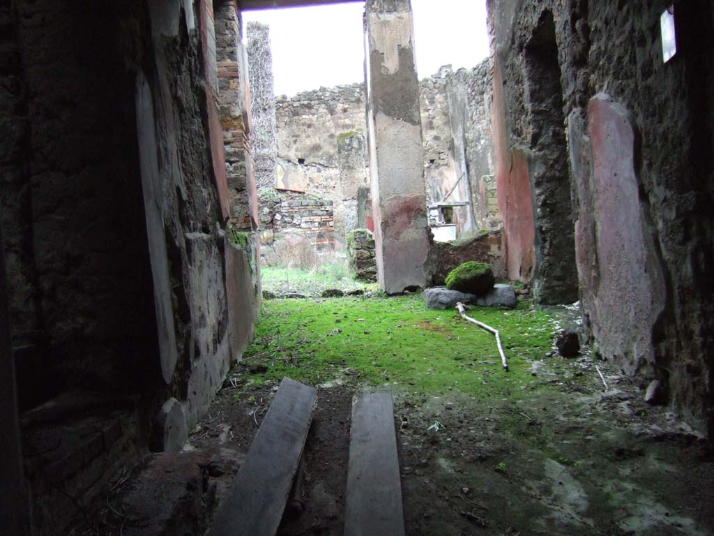 VII.12.28 Pompeii. December 2005. Looking north along entrance corridor towards small garden at the front of the house.
According to Jashemski, this was enclosed on the north and west by a portico supported by three columns and one pilaster.
These were joined by a low wall. At the north-west corner was a small shallow pool in which stood a footed marble basin.
On the pedestal behind the basin stood a marble fountain statuette (see photos below).
On the left corner of the pedestal there was a small bronze head of Jupiter.
See Jashemski, W. F., 1993. The Gardens of Pompeii, Volume II: Appendices. New York: Caratzas. (p.196