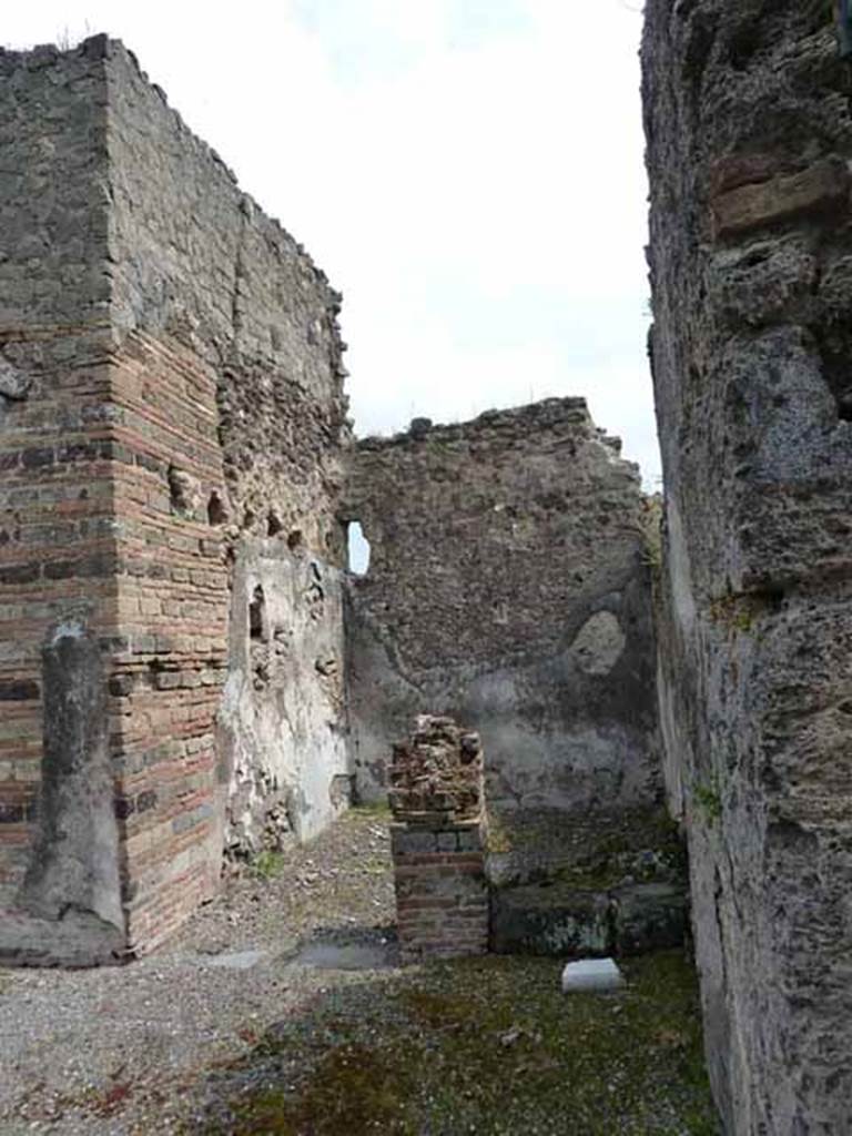 VII.13.4 Pompeii. May 2010. Looking east from entrance towards steps to upper floor and small storeroom.  According to Fiorelli –
A destra si trova la scaletta del piano superiore attigua ad un rustico cubicolo, che altro ne teneva accanto decorato nelle pareti con bustini rinchiusi in circolo, interamente svaniti,e da figurine isolate in mezzo a scompartimenti architettonici, che si riconoscono tuttavia per quelle di Venere pescatrice, di Paride (?) con Amore sull’omero e di Narciso in piedi con Amore allato che si specchia nell’onda. Indi evvi l’ala, che conteneva un grande armadio, e dalla quale entravasi nel cennato cubicolo, nonche in un compreso rustico probabilmente servito per deposito di quel generi, di cui il servo della casa faceva smercio nell’annessa bottega.
(trans.”To the right, one finds the stairs to the upper floor adjoining to a rustic cubiculum, while another nearby was decorated in the walls with heads enclosed in medallions, entirely faded and vanished, and by isolated figures in the midst of architectural decorations, which one could recognize however, as being Venus Pescatrice, of Paris (?) with Cupid on the shoulder and of Narcissus standing with Cupid who was reflected in the water. 
Then there was the ala, which contained a large cupboard, and from which one entered into the indicated cubiculum, the rustic room probably served for storage of those things which the servant of the house sold in the adjoining shop.”)
Fiorelli, G: Descrizione di Pompei, 1875. (p.295-6)