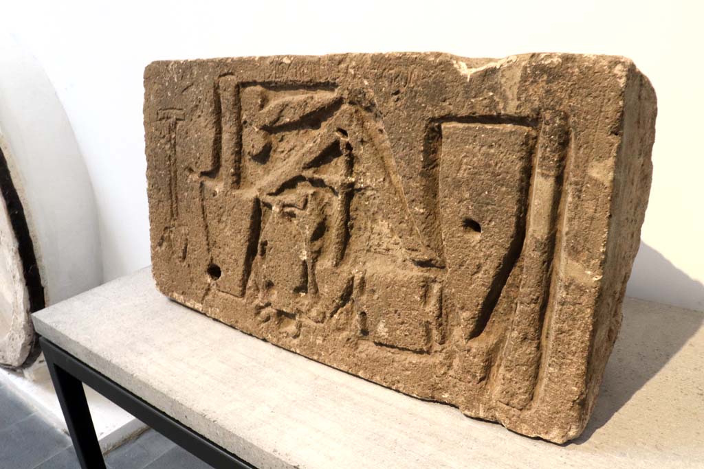 VII.15.1/2 Pompeii. February 2021. 
Limestone relief signed by the master builder (structor) Diogenes depicting –
a trowel, an apotropaic phallus, a plumbline, a cudgel or an axe/a hammer that cuts orthogonally, a scalpel and two unidentifiable objects. 
On display in Antiquarium at VIII.1.4 but found on the west perimeter wall of the house at VII.1.52, on Via dei Soprastanti.
Photo courtesy of Fabien Bièvre-Perrin (CC BY-NC-SA).