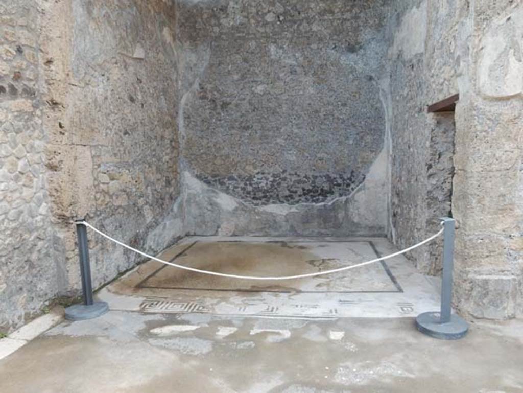 VII.15.2 Pompeii. May 2018. Looking east across ala on east side of atrium. Photo courtesy of Buzz Ferebee. 
This room when discovered was described as “richly decorated with paintings and very well preserved”.
The zoccolo was painted black with architectural motifs and plants.
The middle zone was divided into panels with a yellow background, separated by white compartments in which were painted candelabra topped with eagles on globes, and at the edges were architectural decorations with shields, garlands and sphynx.
In the middle of the south wall would have been the painting with Venus fishing (pescatore).
In the middle of the east wall would have been the painting of Neptune/Poseidon with trident and dolphin.
In the middle of the north wall would have been the painting of Leda and the swan.