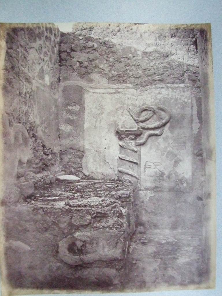 VII.15.13 Pompeii.  Kitchen with altar and Genius Lar relief on east wall.
Old undated photograph courtesy of the Society of Antiquaries, Fox Collection. A Lar can be made out in the top left hand corner, and a hog’s head on the right side of the altar.