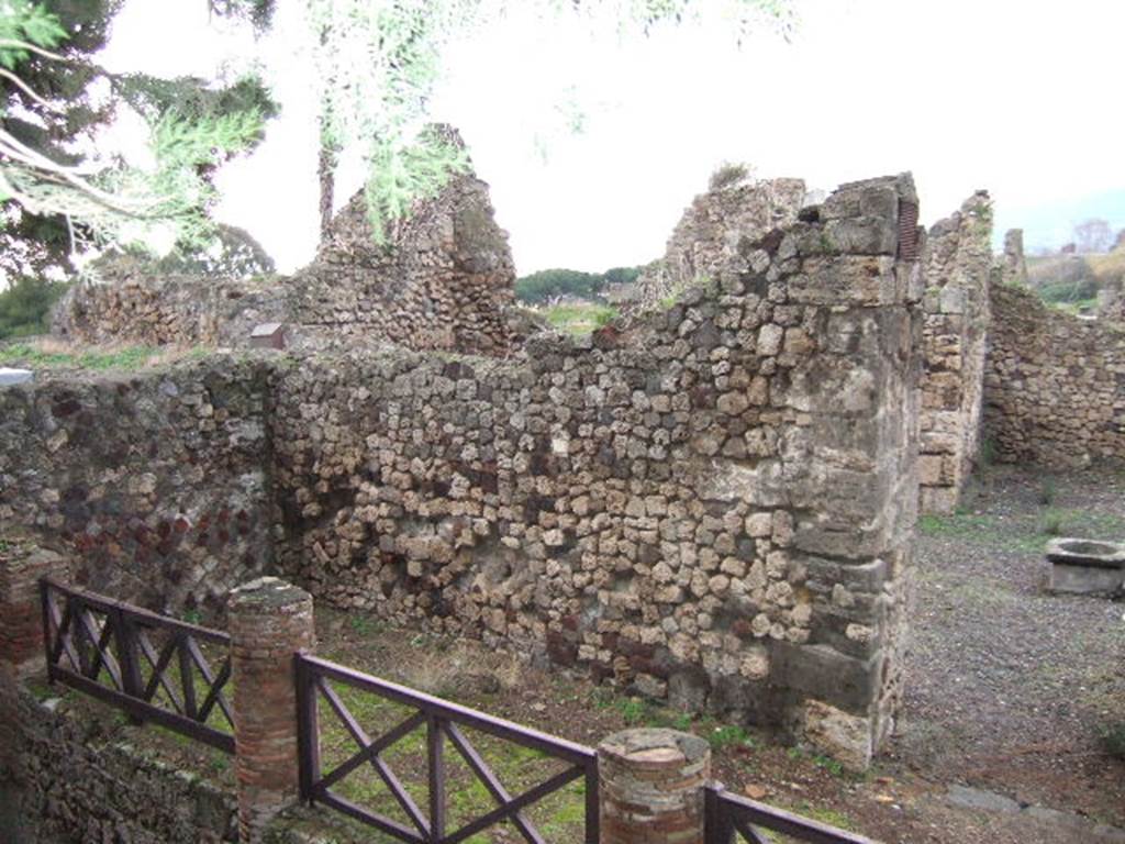 VII.16.1 Pompeii. September 2005. Looking north-west from Temple of Venus towards entrance doorway, on right. On the left behind the wall would have been the area of the portico and peristyle. According to Garcia y Garcia, this house was badly hit by the bombing on 13th September 1943. The bombing totally demolished the atrium, five annexed rooms on the north and east sides, and the portico near the baths.  The impluvium has now totally vanished. In many ways, the restoration of 1950 has changed and distorted the original plan of the house. The stairs on the north-west side of the atrium and the portico have vanished. The baths of the house are now accessible only from no.12. Near the baths was a portico of fourteen columns. The portico does not exist anymore, erased by the bombardment.
See Garcia y Garcia, L., 2006. Danni di guerra a Pompei. Rome: L’Erma di Bretschneider. (p.130-1)
According to Jashemski, the peristyle garden was reached by a short flight of steps, at the left west rear of the atrium. It was enclosed by a portico on the south, east and north, supported by columns.
See Jashemski, W. F., 1993. The Gardens of Pompeii, Volume II: Appendices. New York: Caratzas. (p.201)