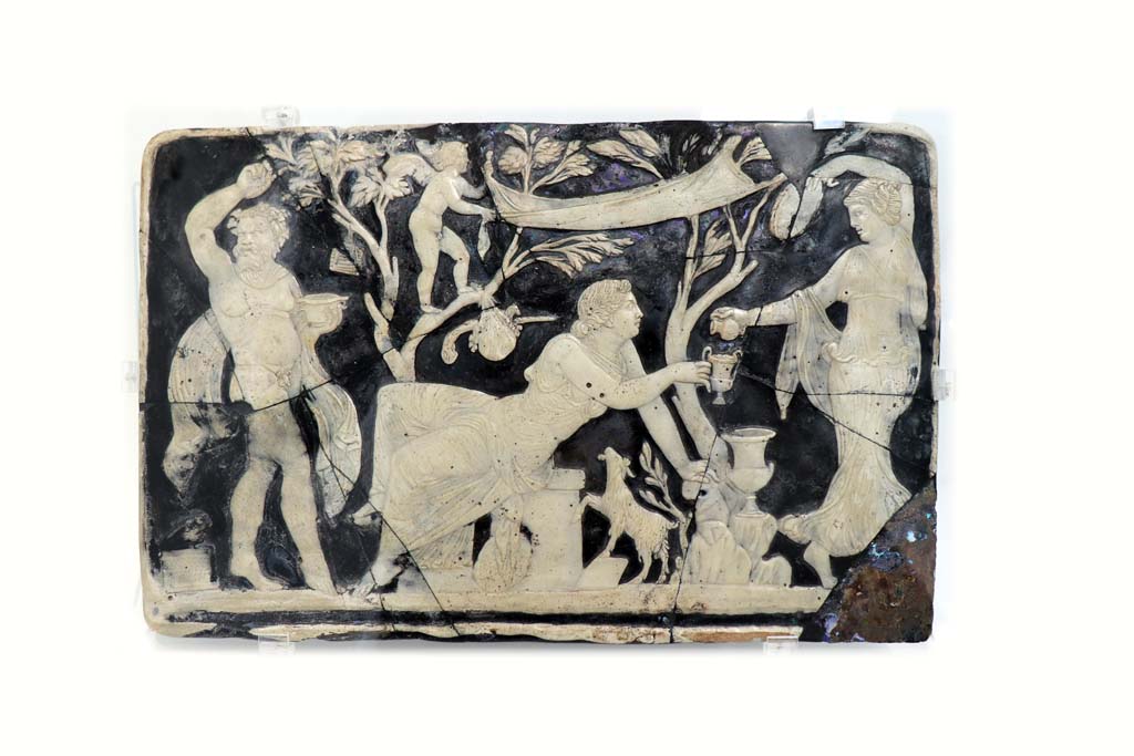 VII.16.22, Pompeii. February 2021. Glass cameo panel decorating furniture, a maenad is pouring wine into Ariadne’s cup while a Satyr dances.  
On display in Antiquarium at VIII.1.4, according to the description card, these were found in room 62. 
Photo courtesy of Fabien Bièvre-Perrin (CC BY-NC-SA).