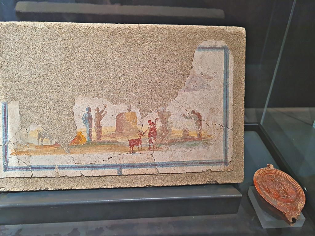 VII.16.a Pompeii. Suburban Baths. March 2024. The exhibition card only says this landscape is from the Suburban Baths. We do not know the exact location.
Photo courtesy of Giuseppe Ciaramella.
Fresco showing Sacred idyllic landscape, 54-68 AD. (Paesaggio idillico sacrale, 54-68 d.C)
On display in exhibition in Palaestra entitled – “L’altra Pompei, vite comuni all’ombra del Vesuvio”.
PAP inventory number 41667.