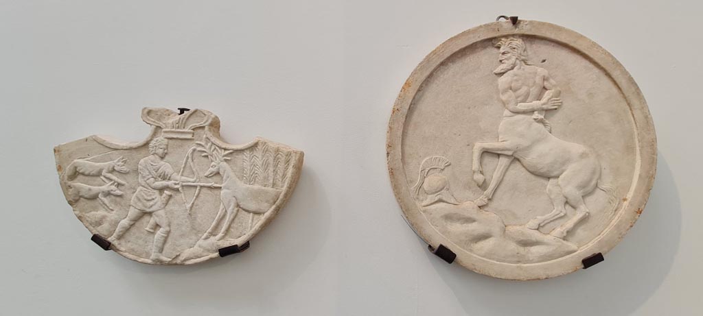 VIII.1.4 Pompeii. April 2022. Decoration (oscilla) hung between columns in the porticoes. Photo courtesy of Giuseppe Ciaramella.
On the left, from I.4.25, Oscilla showing scenes of Hercules’ life.
On the right, from VI.16.7 Oscilla hung between columns in the porticoes, showing centaur.