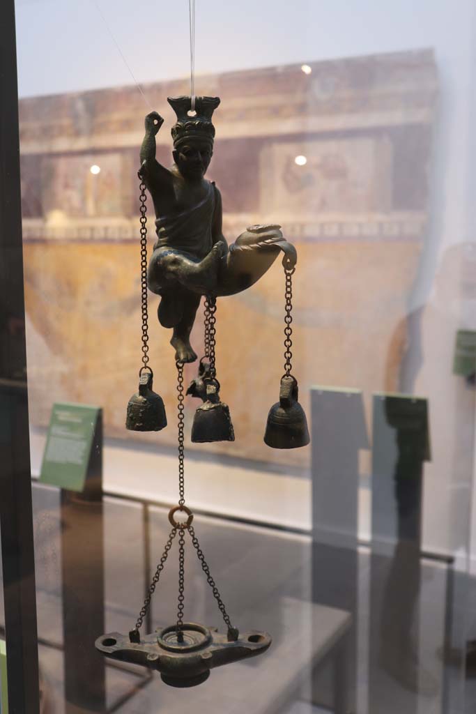 VIII.1.4 Pompeii. February 2021. 
Bronze lamp with statuette of a satyr with a phallus from which small bells hang, found in I.6.3.  
Photo courtesy of Fabien Bièvre-Perrin (CC BY-NC-SA).
