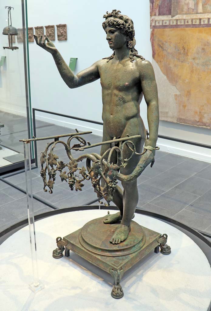 VIII.1.4 Pompeii. February 2021. 
Detail of bronze Ephebus as an oil lamp holder, found in dining room of VII.16.17/22.
The terracotta plaques, on the wall to the left, may have been found during the excavation of the foundations of the Greek temple.
(See p.103, of Fiorelli, G., 1897. Guida di Pompei, Museo Pompeiano terracotta items, below, for more photos).
Photo courtesy of Fabien Bièvre-Perrin (CC BY-NC-SA).
Parco Archeologico Pompei, inventory number 13112.