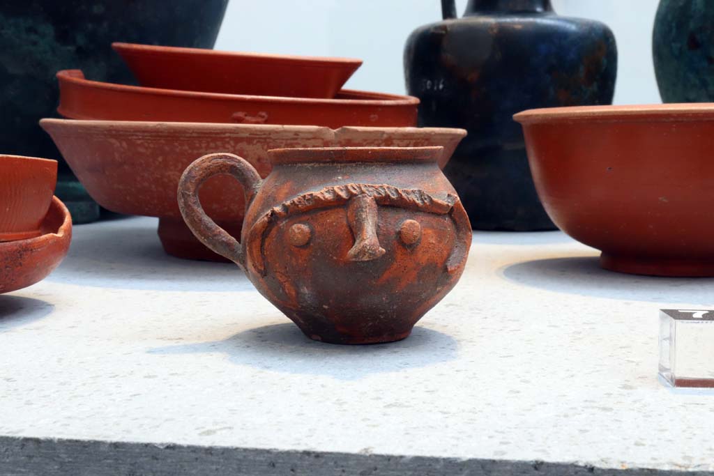 VIII.1.4 Pompeii. February 2021. 
Beaker decorated with indentations and a human face together with red ware plates and bowls, from I.10.4, House of Menander.    
Photo courtesy of Fabien Bièvre-Perrin (CC BY-NC-SA).