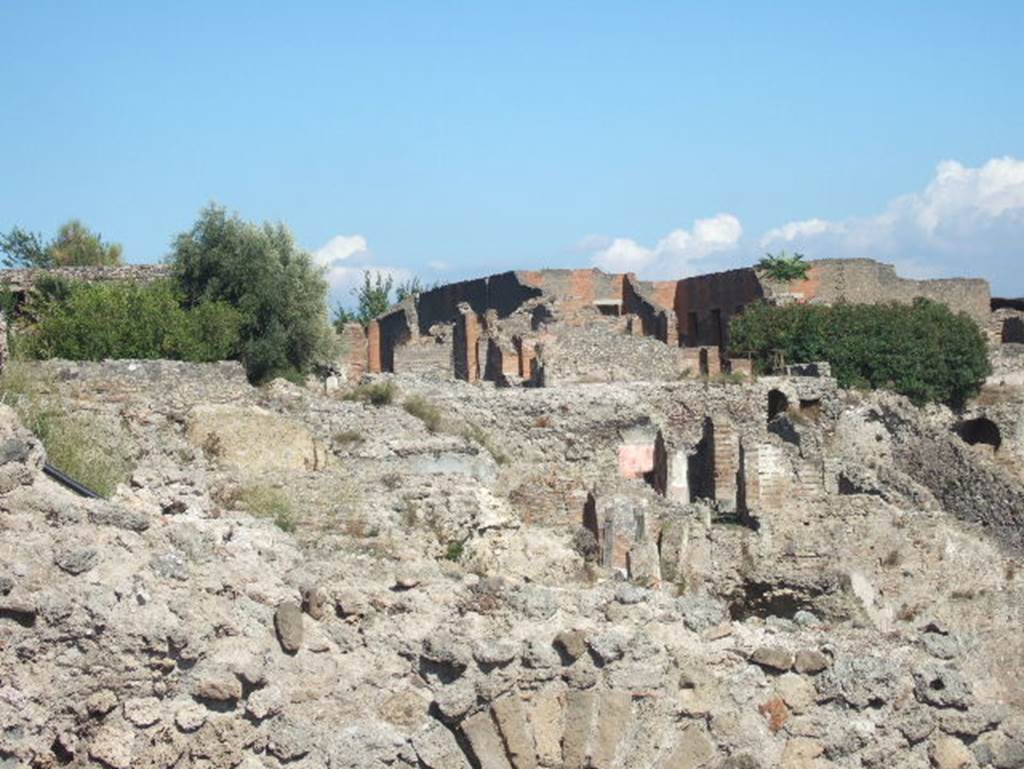 VIII.2.16 Pompeii. September 2004. Looking east towards rear of house at top of slope, and lower levels. Photo taken from exit of site. 
According to PPM – VIII.2.14-16 (p.74 and 75) – regarding rooms on lower levels -
“……and those (rooms) on the west side belonged in reality to the house at nos. 3-5.”
And -
“On the lower level, and reachable by stairs towards the west, were rooms 10-13, which had mosaic flooring and remains of paintings of mediocre quality.
The rooms (14-22), about 3m higher than the rooms 10-13, were probably reachable from the house at no. 3, even if built in the same building phase”.
(For photos taken of rooms 16 and 22, see VIII.2.3, pt.2). 
See Carratelli, G. P., 1990-2003. Pompei: Pitture e Mosaici. VIII. (8). Roma: Istituto della enciclopedia italiana, (p. 74 and 75). 
According to Boyce, in a kind of cave beneath the court located behind the large atrium of number 16, on the extreme edge of the slope was a sacrarium of peculiar nature.
Against the rear wall of a narrow passage was built a masonry seat.
In the wall above it, a vaulted opening led into a small cell hewn out of the rock, with its floor 0.50m below that of the outer passage.
A second masonry seat was built within the cell, back to back with that in the outer passage.
The only means of entrance into this inner chamber appeared to have been over these two seats and through the small opening above them.
Within the cella stood a rectangular masonry altar and upon the altar lay a small terracotta altar, a marble ball, and two lamps decorated with reliefs.
One of the lamps was decorated with the relief of Jupiter, the other of a rose.
See Notizie degli Scavi di Antichità, 1890, 290.
See Boyce G. K., 1937. Corpus of the Lararia of Pompeii. Rome: MAAR 14. (p.74, no.344) 
See Giacobello, F., 2008. Larari Pompeiani: Iconografia e culto dei Lari in ambito domestico. Milano: LED Edizioni. (p.246)