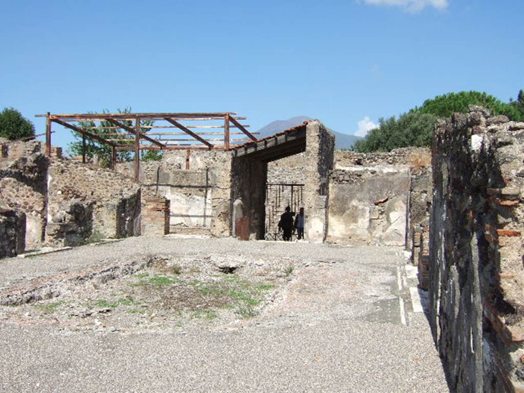 VIII.2.26 Pompeii. September 2005. Looking north across atrium ‘d’ to entrance doorway.
When excavated, the large impluvium was already missing its coating, probably of marble. 
In the centre it would have had a fountain fed by a pipe that entered below the floor in the north-east corner, where the large hole remains unrestored. On the right can be seen the remains of the black floor mosaic with inset large stones of white tesserae and a border of two white lines.