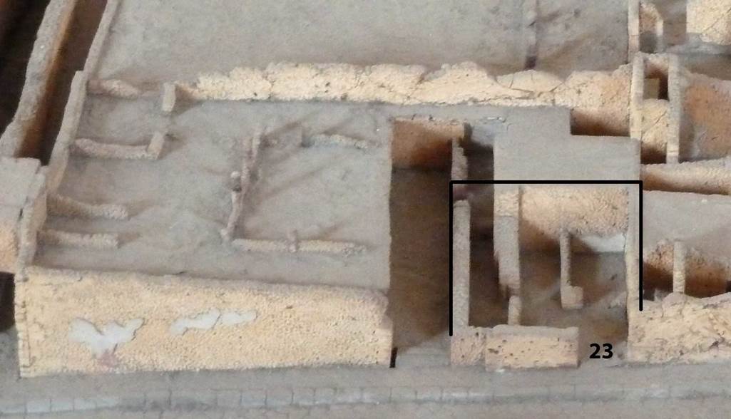 VIII.7.23 Pompeii. Model showing area of the shop, and its location near to VIII.7.22 and VIII.7.24. Model now in Naples Archaeological Museum. According to Fiorelli, this was a shop belonging to the adjoining house, at VIII.7.24. It would have been positioned under the peristyle above. Internally, it had two small rooms, on the west side of the shop.
On the left was the kitchen and perhaps a storeroom. On the right was a latrine adjoining the entrance doorway.  See Pappalardo, U., 2001. La Descrizione di Pompei per Giuseppe Fiorelli (1875). Napoli: Massa Editore. (p.134)