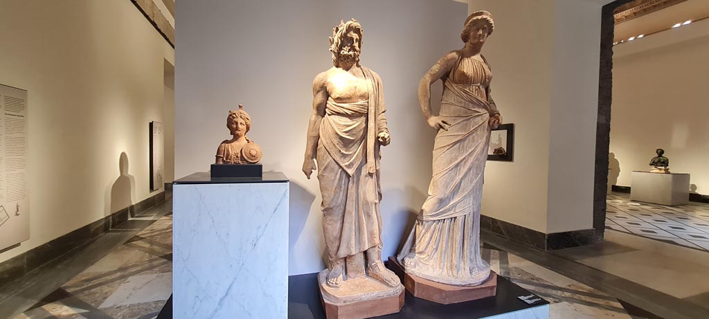 VIII.7.25 Pompeii. April 2023. Three statues found in Temple now said to be of Bellona, Asclepius, and Venus, on display in Naples Museum Campania Romana gallery. 
According to the information card in Naples Museum, the two other statues are closely associated with Asclepius. The female statue has been identified as Venus while the bust depicting an armed goddess has been interpreted as Bellona. The deities were cherished by the dictator Sulla and were added when the temple underwent major restoration in about 70 BC.
Photo courtesy of Giuseppe Ciaramella.