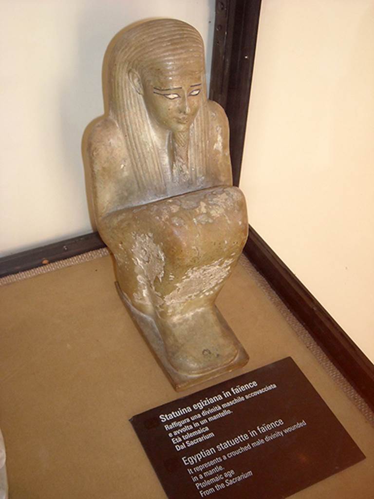 VIII.7.28 Pompeii. Ptolemaic era. Found in the niche on the north wall of the sacrarium.
Egyptian statue in faience representing a crouched male divinity covered in a mantle.
Now in Naples Archaeological Museum. Inventory number 430.