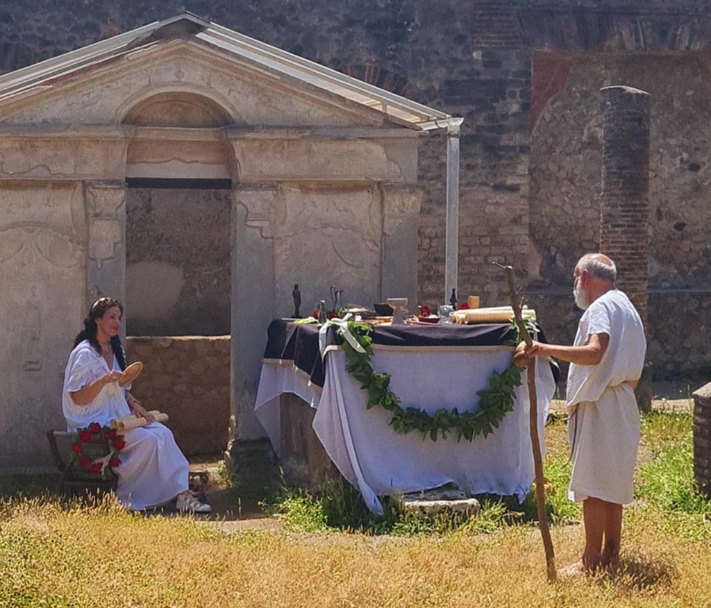 VIII.7.28 Pompeii. 8th June 2024. Actors playing ancient pompeians, and altar dressed with offerings. Photo courtesy of Giuseppe Ciaramella.
Historical reconstruction entitled L’altra Pompei prende vita (The other Pompeii comes to life).