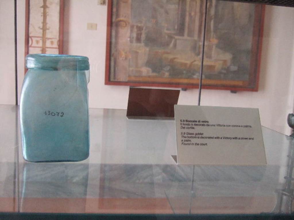 VIII.7.28 Pompeii. Square blue glass bottle with large rim, found in the courtyard. The bottom is decorated with the goddess of victory Vittoria who walks to the left bearing a crown and a palm tree. 
Now in Naples Archaeological Museum. Inventory number 13072.