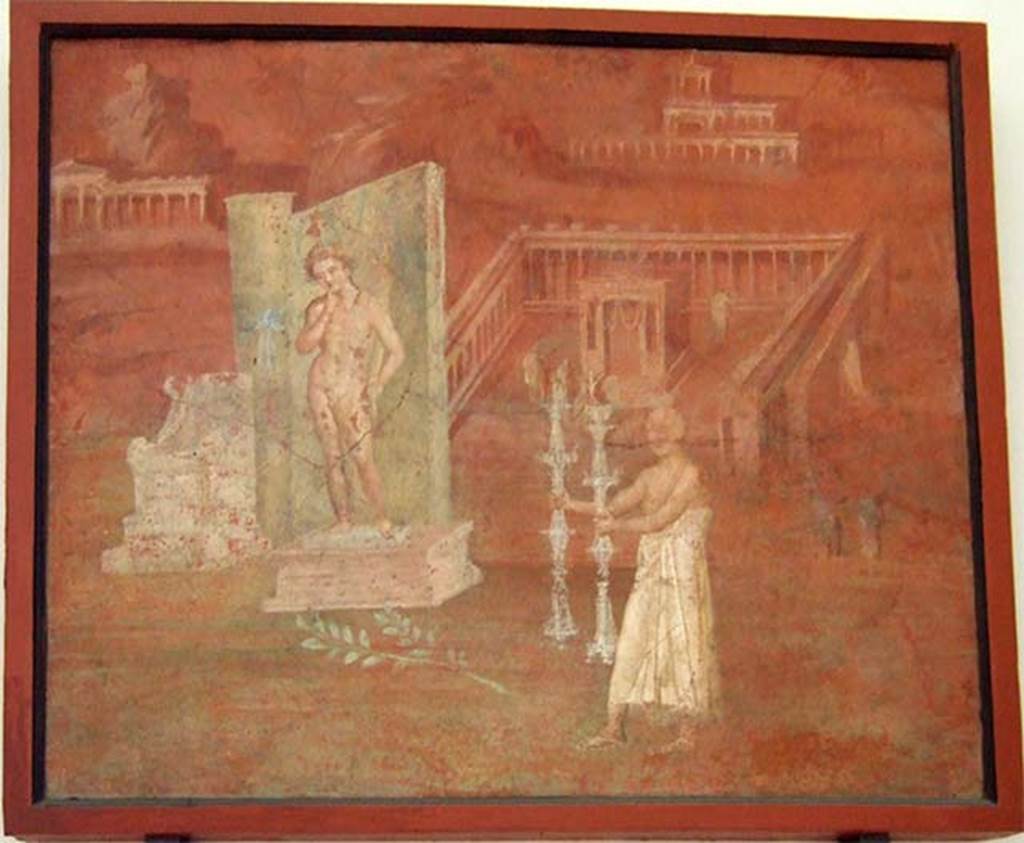 VIII.7.28 Pompeii. Painting found in niche on east wall.
It shows a montage of features concerned with the worship of Isis, including a statue of Harpocrates, a boy with a finger in his mouth holding a cornucopia, with a lotus blossom resting on his forehead. 
Before him stands a priest in a long white robe with a candlestick in each hand. 
In the background is a temple surrounded by a colonnade. 
See Mau, A., 1907, translated by Kelsey, F. W., Pompeii: Its Life and Art. New York: Macmillan. (p. 172).
Now in Naples Archaeological Museum. Inventory number 8975.