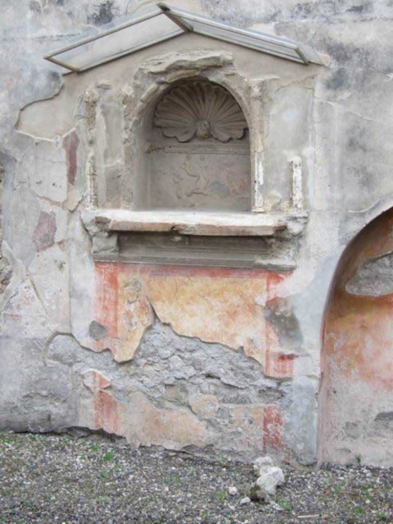 IX.1.7 Pompeii. December 2007. Lararium on south wall of atrium.
According to Boyce,there was a heavy masonry ledge above the panel painted to represent a block of red and yellow variegated marble, bordered in red. It was supported by twin scrolls and ornamented with several bands of stucco relief. On the masonry ledge were the bases of four delicate half-columns, two on each side of an arched niche.
A heavy gable roof used to project from the wall. Within the niche a polychrome stucco cornice runs around the middle of the walls, dividing them into sections, the upper one painted red, the lower one painted blue. On the blue background of the lower section are human figures in stucco relief – now poorly preserved. The arched ceiling is fitted with a shell of stucco. Around the curve of the arch on the wall outside runs another stucco cornice.
See Boyce G. K., 1937. Corpus of the Lararia of Pompeii. Rome: MAAR 14. (p.79, and Pl.6,1).
