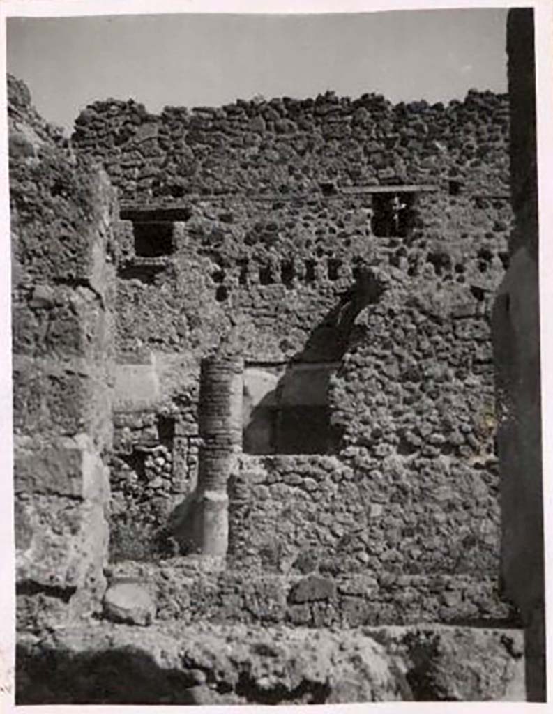 IX.1.12 Pompeii. Pre-1943. Photo by Tatiana Warscher.
Looking across peristyle towards doorway to cubiculum in north-east corner of peristyle. 
According to Warscher, the rear (east) wall had rectangular holes for support beams which demonstrated that there were rooms on an upper floor. 
These rooms would have received light through windows from IX.1.20. 
See Warscher, T. Codex Topographicus Pompeianus, IX.1. (1943), Swedish Institute, Rome. (no.52), p. 82.