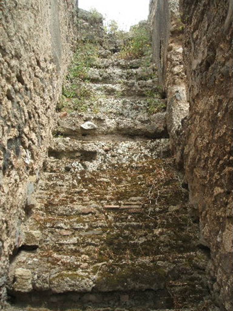 IX.2.27 Pompeii. May 2005. Stairs to upper floor, on east side of peristyle. 
According to Trendelenburg,
“The room adjacent to the triclinium was regarded as a cubiculum, due to a stripe in the floor composed of black and white stones, which indicated the place where the bed would have been. 
Then followed an opening for the stairs, and at the end of this side another room with a spacious entrance. 
See Bullettino dell’Instituto di Corrispondenza Archeologica (DAIR), 1871, p.178