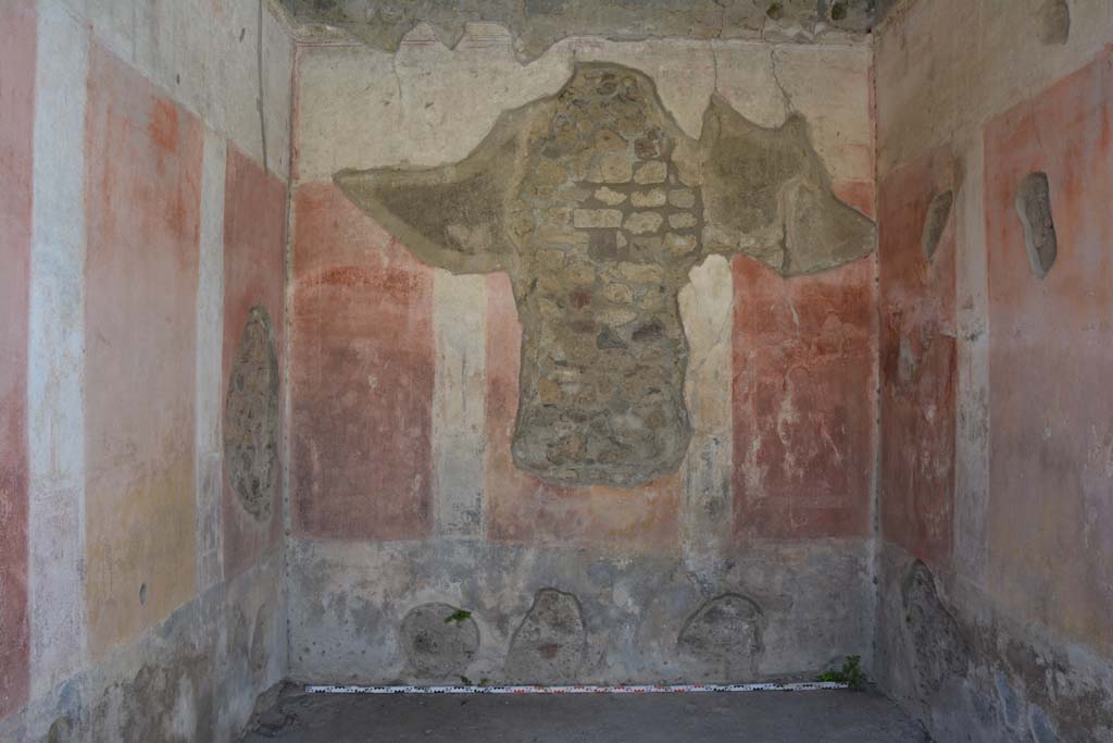 IX.5.11 Pompeii. May 2017. Room e, looking towards west wall.  
Foto Christian Beck, ERC Grant 681269 DÉCOR.
According to Bragantini (1979) –
West wall with hole, the zoccolo was painted black with panels with “carpet” borders of two parallel lines separated by narrow compartments.
The middle zone had a central yellow panel and red side panels.
The upper zone was white with a stucco cornice.
