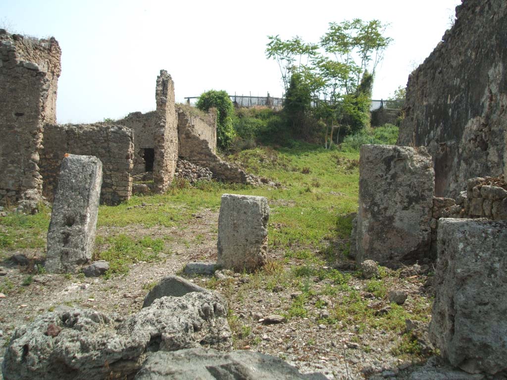 IX.6.4 Pompeii. May 2005. Looking east across site.
The eastern extent of the house can be seen across the centre of the photo, in the middle left.
The pile of stones in the middle centre of the picture, against the north-east wall of the kitchen, would be the site of the hearth, with site of lararium painting above it. 
The wall with a doorway in room “z”, leading to the peristyle of IX.6.5, can be seen in the wall on the left.
According to Garcia y Garcia, during the night bombing of 16th September 1943, the prothyron, the atrium and four nearby rooms adjoining the south and south-west of this house were hit by a bomb. The pavement and street outside were also damaged. 
Another bomb destroyed a good part of the large room on the east of the house and the perimeter eastern wall of the room on the north-east.
See Garcia y Garcia, L., 2006. Danni di guerra a Pompei. Rome: L’Erma di Bretschneider. (p.153).