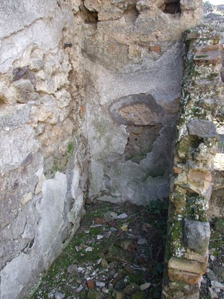 IX.9.e Pompeii. March 2009. Room 16, light yard, south-west corner. Looking west. According to Boyce, in the small open courtyard in the centre of the house, a sacrarium was formed. It was constructed by building a small wall parallel to the south wall, and then covering the enclosure with a sloping roof. At the east end of this enclosure stood a small altar of tufa, originally coated with stucco. The inside surface of the north wall was decorated with a white background and a drawing.
This was of an aedicula and within it a male figure, standing, clad in a yellow tunic. The south wall was also covered with white stucco, the west wall with a coarser variety. A female head of terracotta was found near the sacellum, apparently part of a statue. Not. Scavi, 1889,136; 1891,255.  See Boyce G. K., 1937. Corpus of the Lararia of Pompeii. Rome: MAAR 14. (p.92, no.464 )
