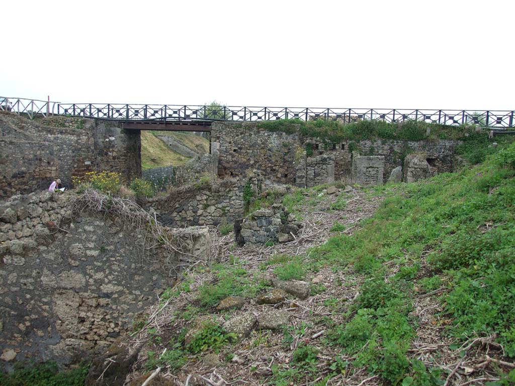 IX.10.2 Pompeii. May 2010. Looking east from IX.10.1 across to IX.10.2 room 5, cubiculum 8, cubiculum 7 and cubiculum 6.
The fence to the right of the modern bridge shows the line of the now covered unnamed vicolo on the east side of the insula.