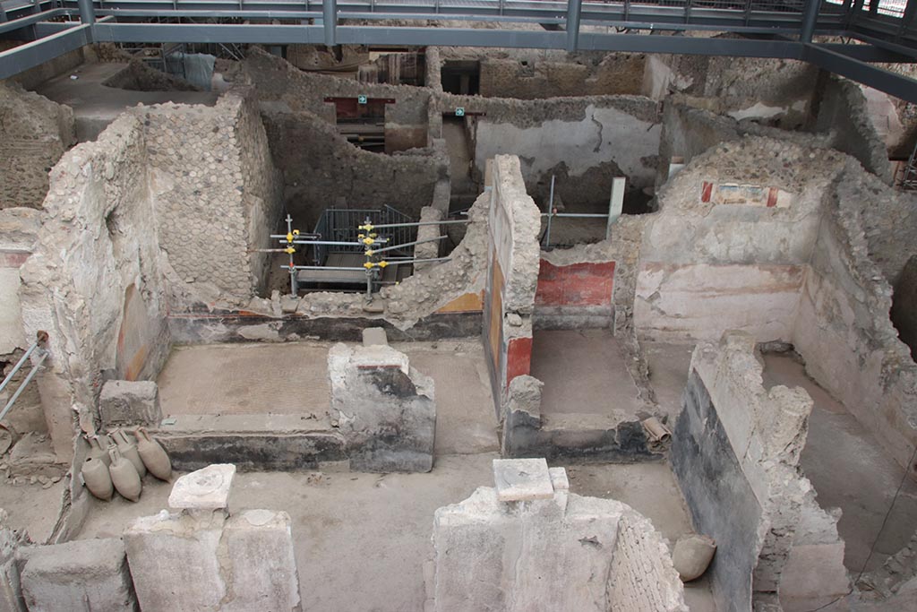 IX.12.4 Pompeii. October 2024.
Looking east towards room “o”, on left, room “l(L)” with red painted walls, centre right, and room “f”, on its south side, on right.
On the upper east wall of room “f”, the painting described as from the zoccolo of an upper room, can be seen.
Photo courtesy of Klaus Heese.