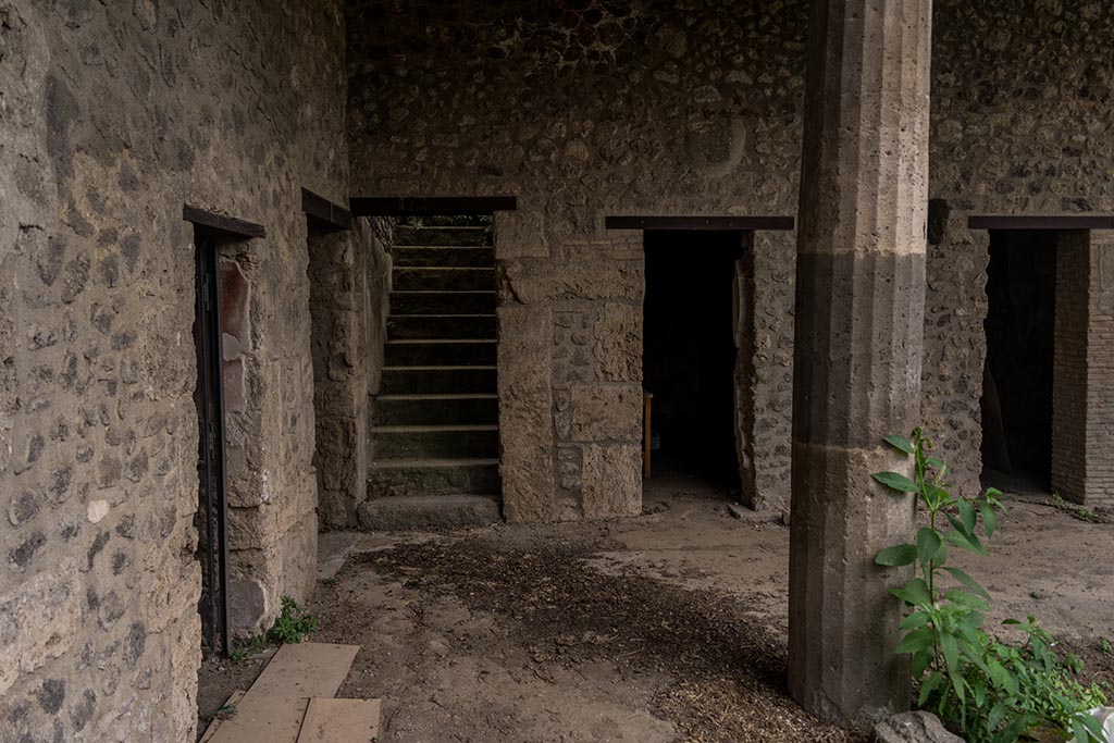 IX.14.4 Pompeii. July 2024. 
Looking west in south-west corner of peristyle with steps to upper floor, and room 12, in centre. Photo courtesy of Johannes Eber.