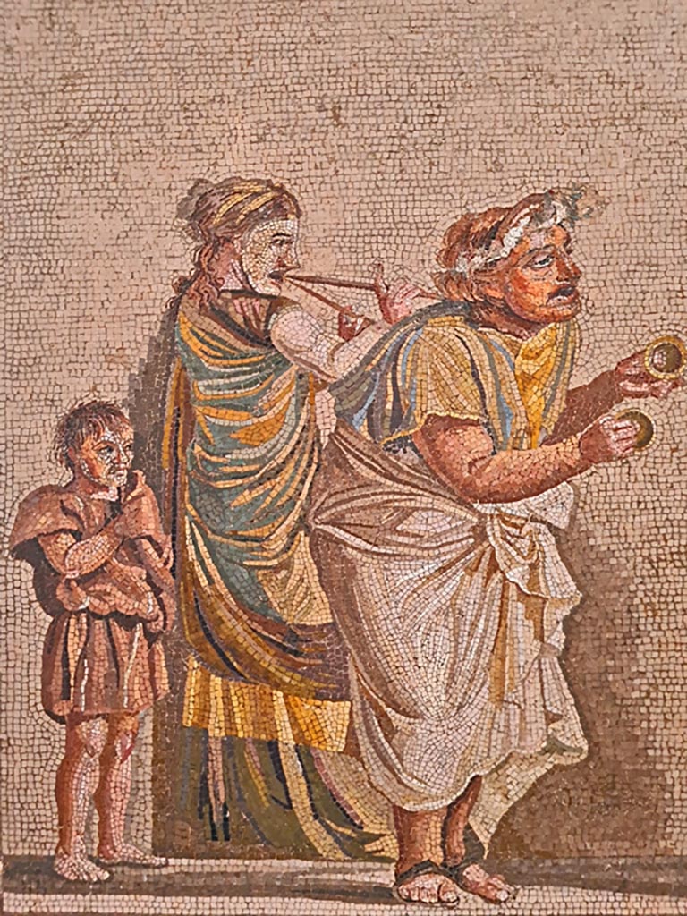 HGW06 Pompeii. Found on 8th April 1763. Ambiente 13 of Villa of Cicero. 
Detail from mosaic of a Group of Street Musicians – 
a musician playing cymbals on the right, in the centre a woman with a double flute, and on the left, a boy follows the procession.
Now in Naples Archaeological Museum. Inventory number 9985.
Photo courtesy of Giuseppe Ciaramella. September 2024.