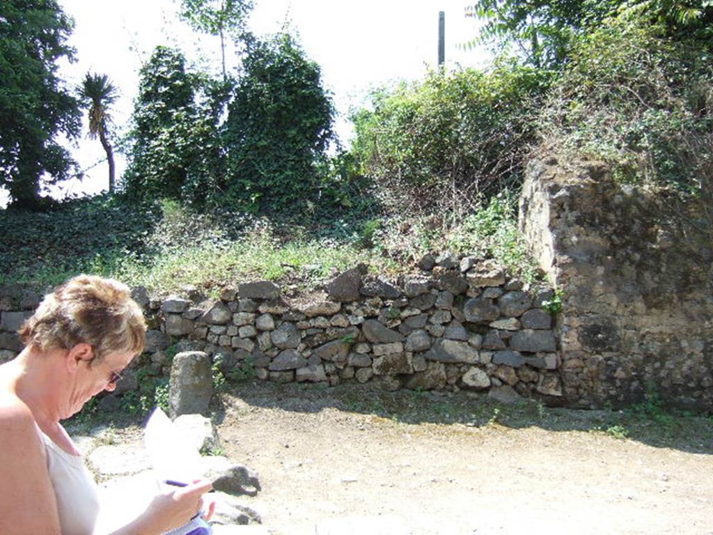 HGW06 Pompeii. May 2006. North side of entrance. According to Spano, found immediately to the left of the shop numbered 7, was a large block of material. This was found during a small excavation in the area, and can be seen on the right of the above photo. This large square mass of material contained a large circular basin, open above. This must have collected in the rain water which flowed from the high part of the Villa of Cicero, at the rear.
This basin, which had already been drawn by Mazois, was only entirely emptied of its eruptive material by this excavation. Finished with sturdy opus signinum, it was formed by an empty cylinder (1.90m deep, and 2.65m wide).The base was rather concave, and in it (to the south-east) was a distribution channel for the water.See Spano in Notizie degli Scavi, 1910, p.268-9.