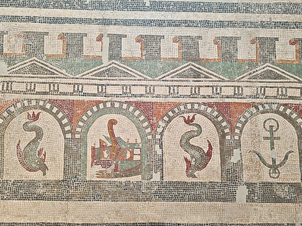 Villa of Diomedes ? or VI 17.10 Pompeii ?. June 2024.  
Detail from mosaic of “doors”, starting with one dolphin, and a stern of a ship with rudder, another dolphin and an anchor.  
On display in Naples Archaeological Museum, Room CXXXIV.  Photo courtesy of Giuseppe Ciaramella.