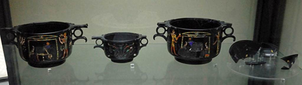 Villa San Marco, Stabiae. Found in room 37, May 1954, near the south east wall. 
Three obsidian Skyphii (cups) with Egyptian scenes inlaid in gold and mosaic and fragments of a phiale (broad flat container) with Nilotic scenes.
From left to right they are Skyphos A, C, B and the phiale.
Photographed December 2007 in Naples Archaeological Museum. Inventory numbers 294471, 294472, 294473 and 294474.
See Barbet A. (a cura di), 1999. La Villa San Marco di Stabia: Illustrazioni 1. Roma, L’Erma di Bretschneider. Figs. 717 to 723.
See Elia O., 1957. Le coppe ialine di Stabia, in BdA, 42. pp. 97-103.