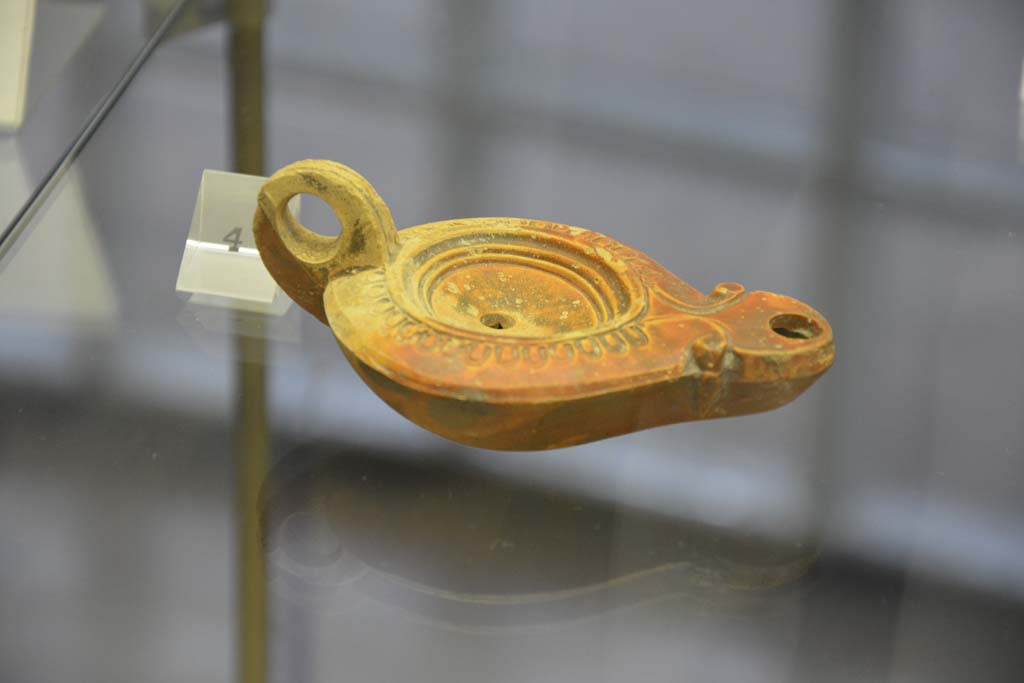 Villa Regina, Boscoreale. April 2017. Above, no.4, terracotta one-handled single flame lamp. Photo courtesy of Adrian Hielscher.
Villa Regina, Boscoreale, (from information card) –
The terracotta lamps found in the villa are of a one handled type, with a beak from which the flame shone. On the bronze support would have leaned the lamp. 
A lamp, which bears a cross sign on the external base, documents the human presence in the area of the villa after the eruption of 79AD.
Le Lucerne fittili rinvenuti nella villa sono di tipo monolicne, ad un becco da cui fuoriusciva la fiamma. Sul sostegno di bronzo veniva poggiata la lucerna.
Una lucerna, che reca sul fondo esterno un segno a croce, documenta la presenza umana nell’area della villa dopo l’eruzione del 79AD.
No.3 (not photographed). A bronze support for a lamp, found in room 2, dateable from Ist century AD.
Nos. 4-6. One-handled lamps, made of terracotta, dateable from 1st century AD.
No.7 (not photographed). A one-handled lamp, made of terracotta, dateable from II to IV century AD.