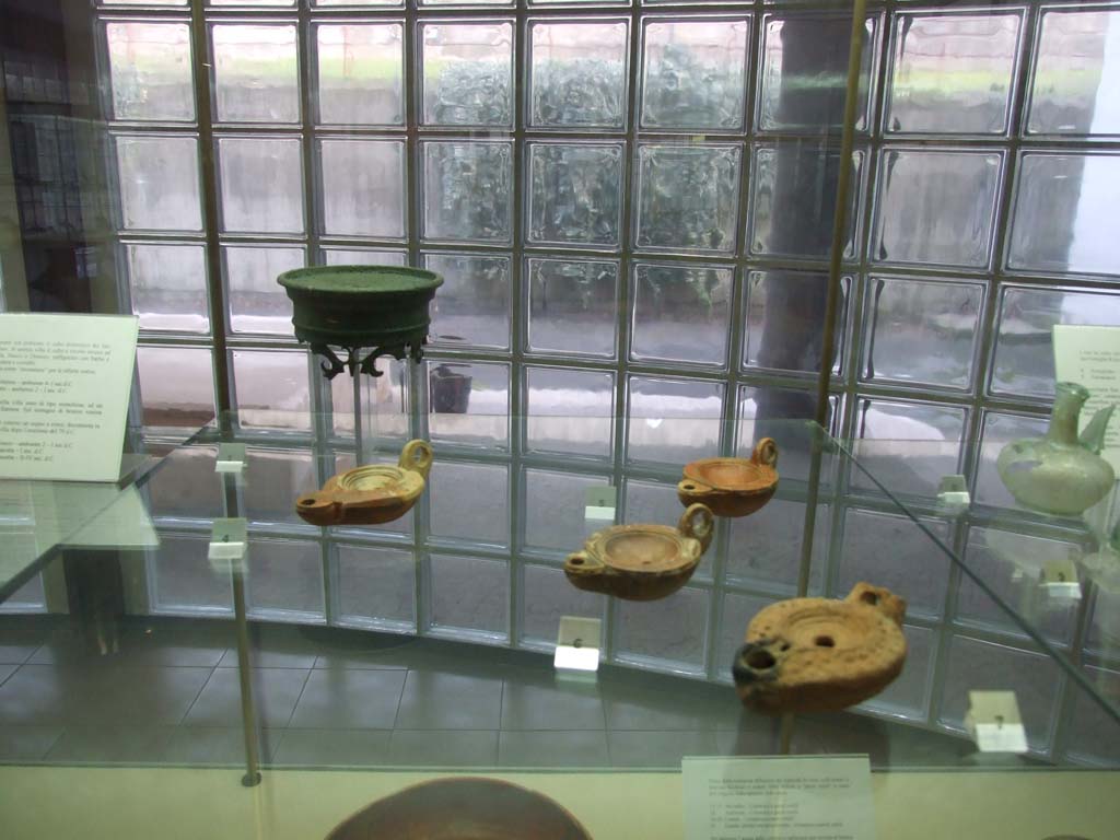Finds from Villa Regina Boscoreale. December 2006. Now in Boscoreale Antiquarium.
A bronze lamp support from storeroom XII.
Three round handled terracotta lamps.
At the front is a terracotta lamp marked with a cross on the outside.
According to the Antiquarium, this is a Christian lamp, dated to 2nd-4th century AD, and shows a sporadic presence on the site after the 79AD eruption.