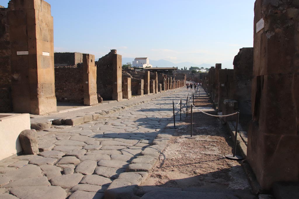 Via dell’Abbondanza, Pompeii. October 2022. 
Looking east between VII.13, on left behind fountain, and VIII.5, on right. Photo courtesy of Klaus Heese.