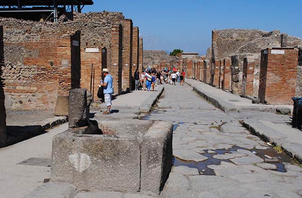 Via dell’Abbondanza. July 2012. Looking east towards junction with Via del Lupanare, on left, and Via dei Teatri, on right. Photo taken from near fountain at VII.14.13/14. Photo courtesy of John Vanko. His father took the identical photo in February 1952, see below.