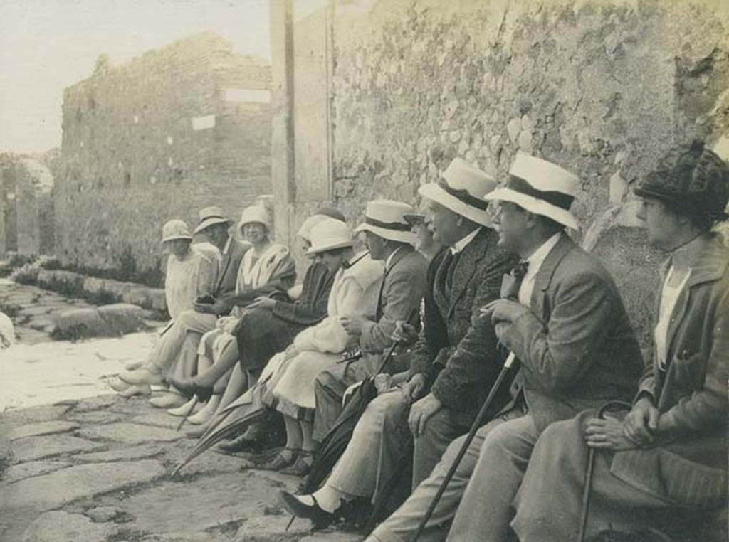 Vicolo Storto, Pompeii. 5th June 1925. Tourists having a rest sitting on the high pavement on the west side of the vicolo. On the left is the junction of Vicolo Storto, with the Via degli Augustali, and on the opposite side of the roadway is the Vicolo di Eumachia. Photo courtesy of Rick Bauer.