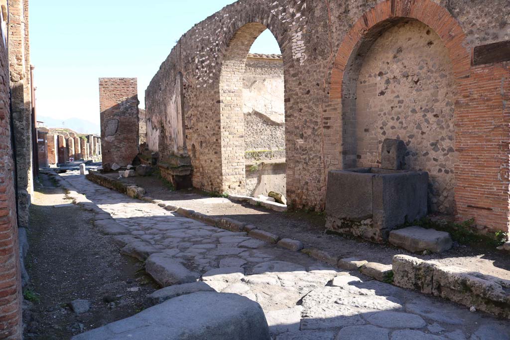 Vicolo dei Soprastanti, south side, December 2018. 
Looking east along VII.8, north wall of Forum, and fountain at side of entrance to the Forum. Photo courtesy of Aude Durand.