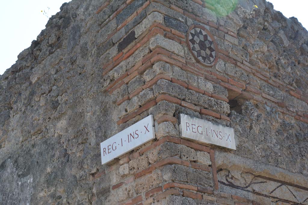 Vicolo del Citarista, April 2017. 
Corner of insula I.10, Vicolo del Menandro, on left, and coloured terracotta plaque above doorway of I.10.9, in Vicolo del Citarista, on right.  
Photo courtesy Adrian Hielscher.
