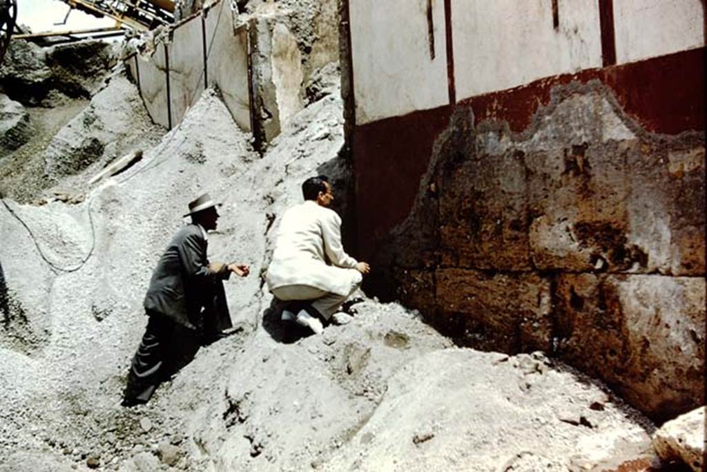 Vicolo di Ifigenia, east side, Pompeii. 1961. Studying the wall on the south side of doorway at III.4.e.  Photo by Stanley A. Jashemski. 
Source: The Wilhelmina and Stanley A. Jashemski archive in the University of Maryland Library, Special Collections (See collection page) and made available under the Creative Commons Attribution-Non Commercial License v.4. See Licence and use details.
J61f0300