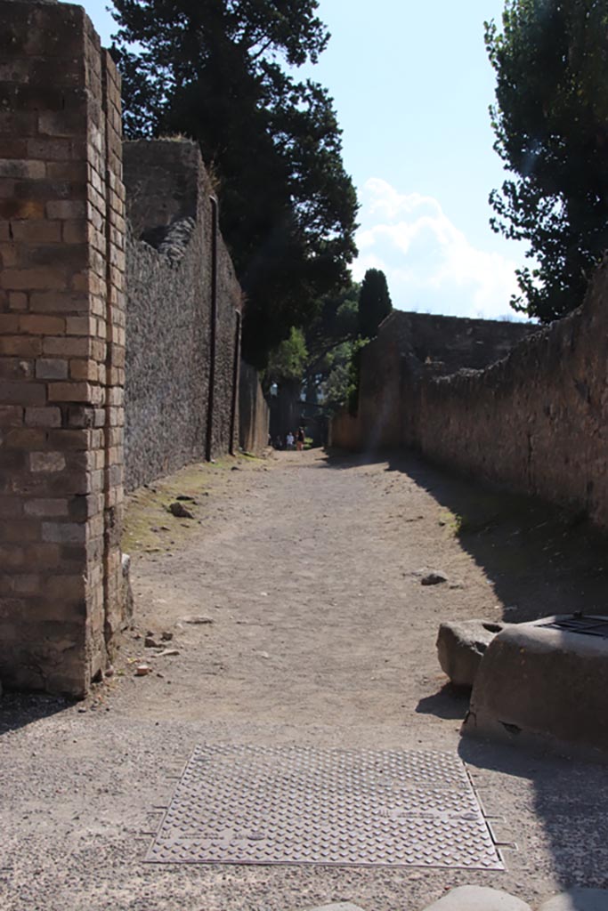 Vicolo di Octavius Quartio, Pompeii. October 2022. 
Looking south from junction with Via dell’Abbondanza. Photo courtesy of Klaus Heese.
According to Della Corte –
“The narrow street to the south that has been excavated in the eastern half of its entire length, was rendered on its entrance impervious to vehicular traffic by joining the two footpaths, and closed by a door of which remain in situ, all certain elements, close by a water-castle (castellum aquae privatum). This sustains also today its lead water reservoir with one of the pipes (fistulae aquariae) going down from the bottom of the reservoir. At a short distance and nearly outside the footpath, there is to be seen a large lead belled chest of the aqueduct, upon a pipe of which is inserted a large bronze arrest-key. On the left of the water-castle is a cross-way public altar in honour of some Gods impossible to be identified today in the faded painting.”
See Della Corte, M. Pompeji, the new excavations – houses and inhabitants 1925. (p.67).
According to Garcia y Garcia, the north end of the vicolo between II.2 and II.1 was hit heavily by the bombing of 19th September 1943.
The pilaster, with the lead container for water on top, was completely destroyed.
This was a unique example from Pompeii, the only one so far discovered here.
See Garcia y Garcia, L., 2006. Danni di guerra a Pompei. Rome: L’Erma di Bretschneider. (p. 44, figs. 37-39)