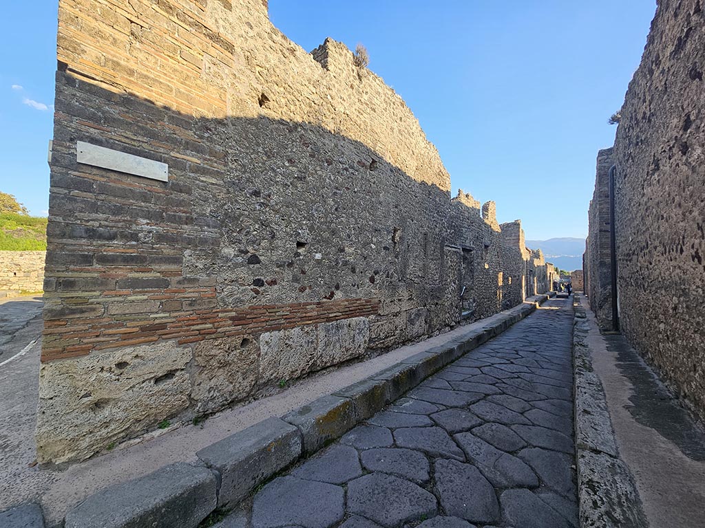 Vicolo di Tesmo, Pompeii. November 2024. 
Looking south along east side towards doorway into IX.7.21, from junction with unnamed vicolo (continuation of Via degli Augustali) on left. 
Photo courtesy of Annette Haug.