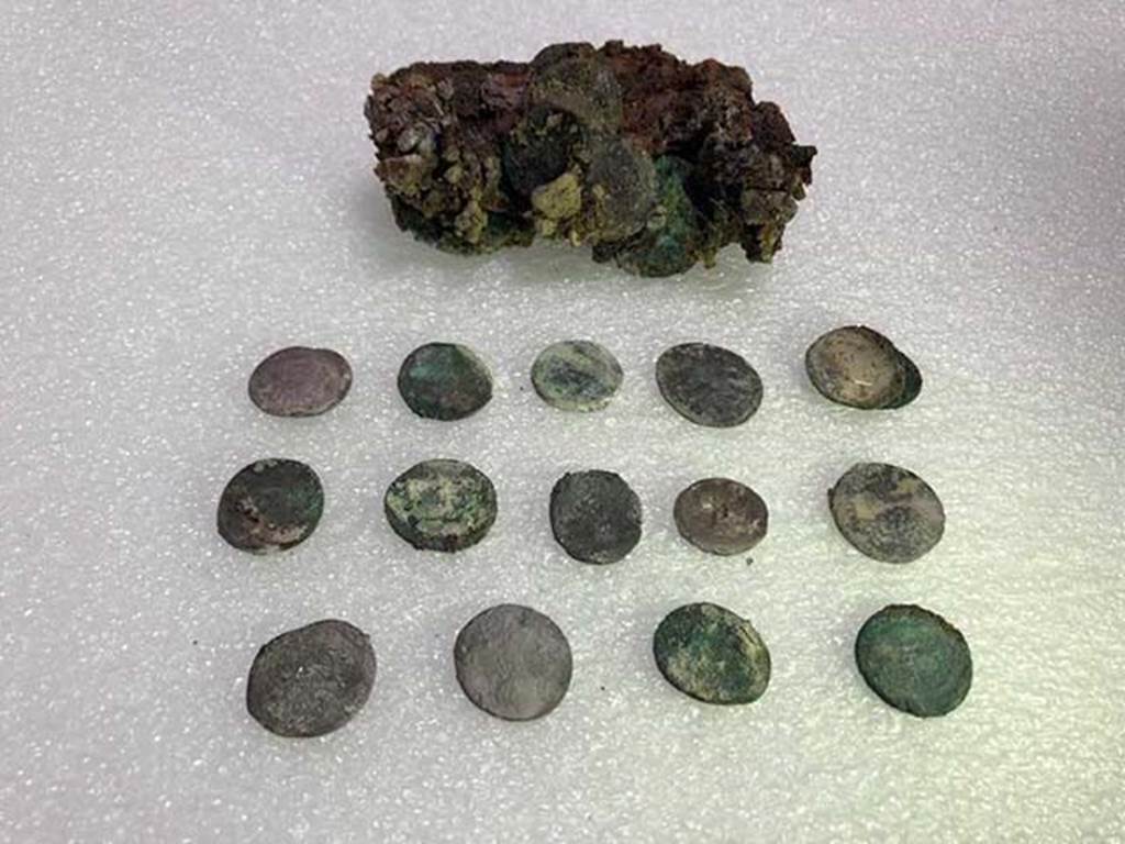 Vicolo delle Nozze d’Argento with the Vicolo dei Balconi intersection. Leather pouch containing coins found under Pompeii skeleton.
At first examination there would seem to be at least 20 silver denarii and two bronze asses with a nominal value of eighty sesterces and a half. 
Such a quantity of coins could at that time guarantee the maintenance of a family of three for 14 to 16 days.
The coins have a very varied chronology. It was possible to examine 15 coins, for the most Republican, starting from mid-2nd century BC.
One of the later Republican coins, is a Legionary Denarius of Mark Antony, common in Pompeii, with the indication of the XXI legion. 
Among the few identified imperial coins, a probable denarius of Octavian Augustus and two denarii of Vespasian.
Photograph © Parco Archeologico di Pompei.